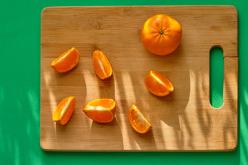Pieces of mandarin on a wooden board in the morning rays of the sun, on a green background