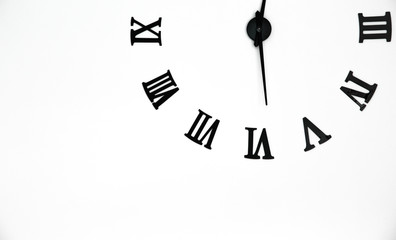 Black clock  with roman arabic numerals and clock hands on white concrete wall background ,  copy space