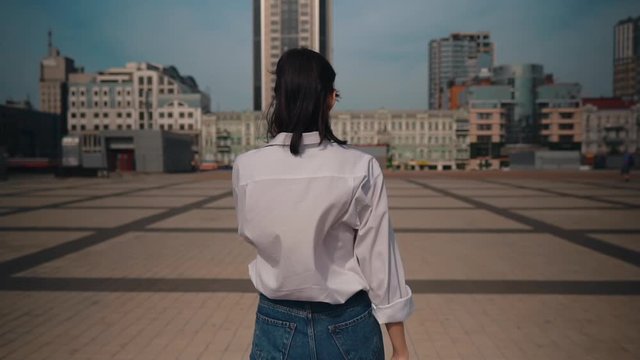 back view student in casual shirt and jeans talking by phone walking in summer city slow motion