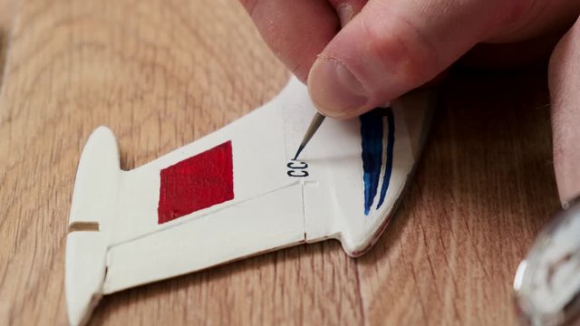 man writes logo letters on wooden tail unit of passenger jetliner model with black color at table extreme closeup slow motion