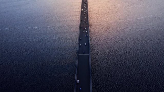 High aerial overhead of traffic over the Tasman bridge across the wide flowing Derwent river in Tasmania Australia, with bike, cars and trucks, crossing at a glowing sunset - dark to light.
