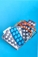 A small shopping basket filled with blisters of tablets on a blue background. Concept for the theme of the sale / purchase of drugs.