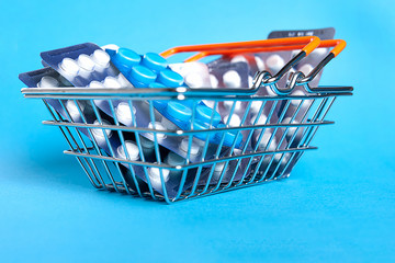 A small shopping basket filled with blisters of tablets on a blue background. Concept for the theme...