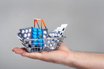 A small shopping basket filled with blisters of tablets on a male hand. Purchase of drugs concept.