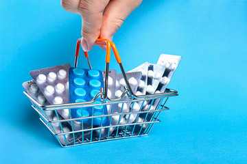 A small shopping basket filled with blisters of tablets, a male hand holds in fingers. Purchase of drugs concept. 