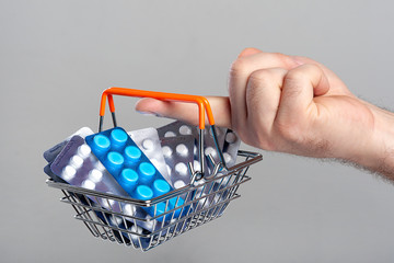 A small shopping basket filled with blisters of tablets on the finger of a male hand. Concept for the theme of the sale / purchase of drugs.