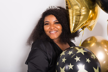 Naklejka premium Holidays, birthday party and fun concept - Portrait of smiling young African-American young woman looking stylish on white background holding balloons.