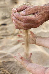 Old man hands sand running into baby hands