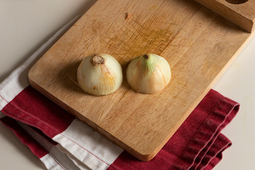 Cebolla blanca partida en la mitad y sobre una tabla para picar con trapo rojo y blanco para preparar comida casera