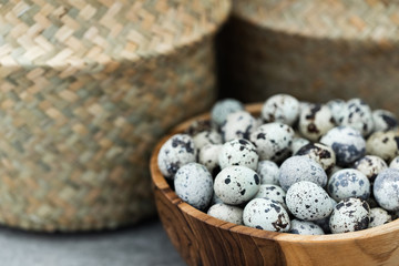 Wooden bowl with heap of small quail eggs on kitchen. Wicker straw basket on background. Empty place for text.