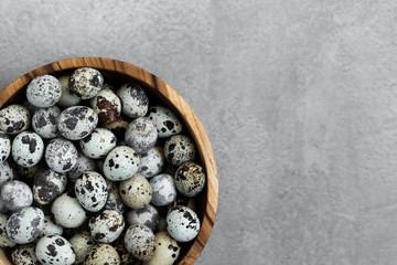 Wooden bowl with heap of small quail eggs on gray concrete background. Empty place for text. Copy space.