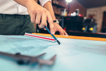 engineers holding a pen pointing to a building and  drawing outlay construction plan as guide for...