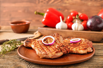 Plate with cooked pork steaks on table