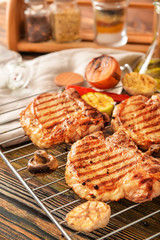 Rack with cooked pork steaks and vegetables on table