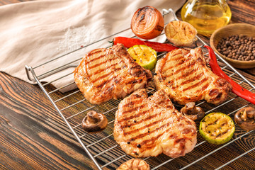 Rack with cooked pork steaks and vegetables on table