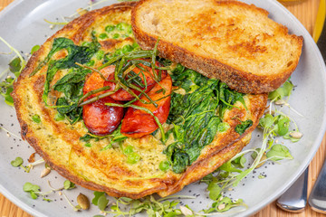 A breakfast setting of Green Egg Omelette with Pesto, Spinach, Peas and Grilled Chorizo