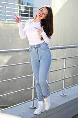 Photo of a caucasian brunette girl in a white blouse and blue jeans stands near the railing with a...