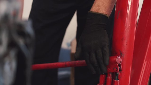 Person wears black gloves. Man wears dark uniform. Worker moves red construction.