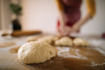 Baking homemade bread. Selective focus of dough on kitchen table with cropped silhouete of woman wearing apron in background