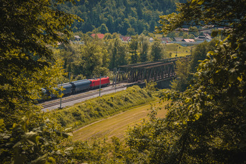 European freight train with red locomotive is driving on a two track railway line towards a metal...