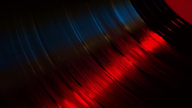 A fragment of a rotating vinyl record in the red rays of a disco. Audio equipment for dj. The moment of a spinning vinyl plate. Turntable vinyl record player
