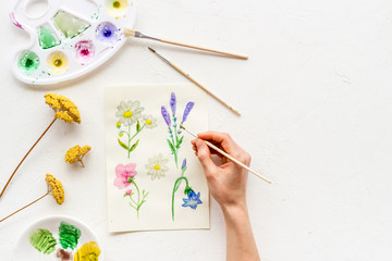 Painting. Female hands draw flowers on white background top-down copy space