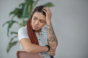 Long-haired with a tattoo on her arm looking unhappy