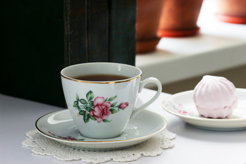 Tea in a vintage cup, marshmallows on a vintage saucer and old books on a light background.