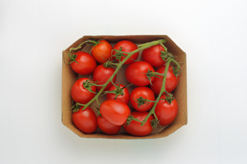Cocktail tomatoes on the branches lie in a cardboard box. Light gray background. View from above.