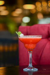 Cold summer alcohol cocktail with ice and fruit in a tall glass on light blurred restaurant or cafe background.