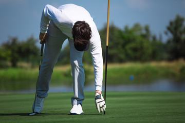Obraz premium Professional golfers pick up golf balls in the holes, golf clubs in their hands, white and black golf gloves, hats and white golf shoes.