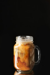 Mason jar with iced coffee on dark background