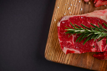 Fresh raw steak on wooden cutting board over black background with spices, top view.