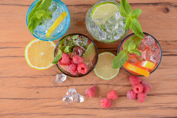 Four tropical mixed drinks, orange, lemon and raspberries cocktails served on light wooden table.