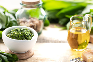 Wild leek pesto with olive oil and parmesan cheese in a white ceramic mortar on a wooden table. Useful properties of ramson.