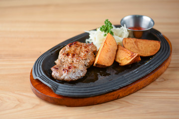 Grilled steak with vegetables and tomato sauce served on a black plate over light rustic background. Baked potato.