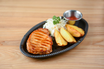 Grilled steak with vegetables and tomato sauce served on a black plate over light rustic background. Baked potato.