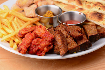 Big plate of beer snacks. Crispy fried chicken, french fries and different kinds of bread on white plate.