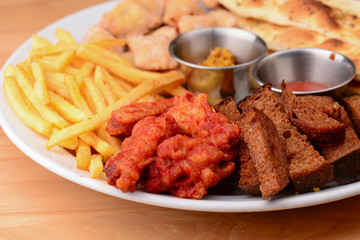 Big plate of beer snacks. Crispy fried chicken, french fries and different kinds of bread on white plate.
