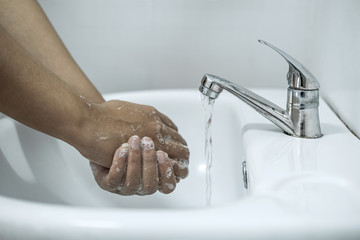 Woman washing hands under the water tap in bathroom with using soap gel for cleaning and prevention...