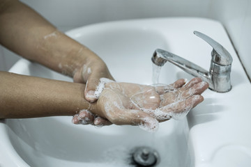 Woman washing hands under the water tap in bathroom with using soap gel for cleaning and prevention inflection coronavirus