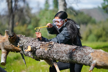 Woman shooting slingshot over forest log, with protective eyewear