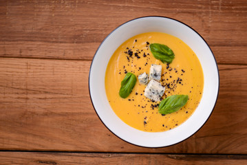 Creamy pumpkin soup topped cheese in a white bowl on a wooden table. Restaurant photography concept. Copy space.