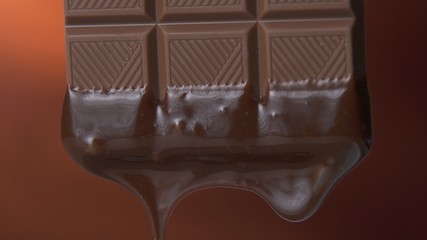 Chocolate bar with melted dark chocolate dripping on a brown background