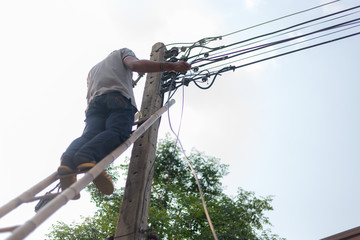 Person climbs electric poles to install electrical and internet cables for use in the home.