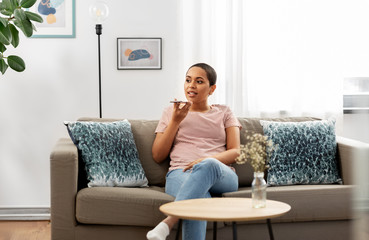 people, technology and communication concept - happy young african american woman using voice command recorder on smartphone at home