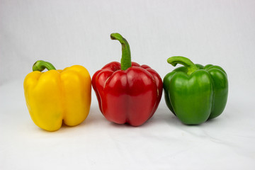 Three bell peppers, red, yellow and an orange one with white background