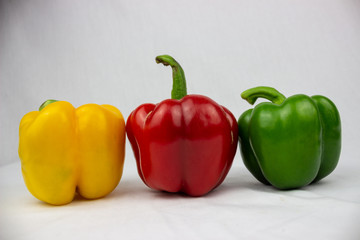 Three bell peppers, red, yellow and an orange one with white background