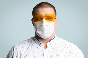 Positive young man wearing  in  yellow sunglass  and  hygienic mask to prevent infection, airborne respiratory illness such as flu, 2019-nCoV on  blue isolated background. 