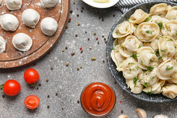 Cooked and raw tasty dumplings with sauce on grey background